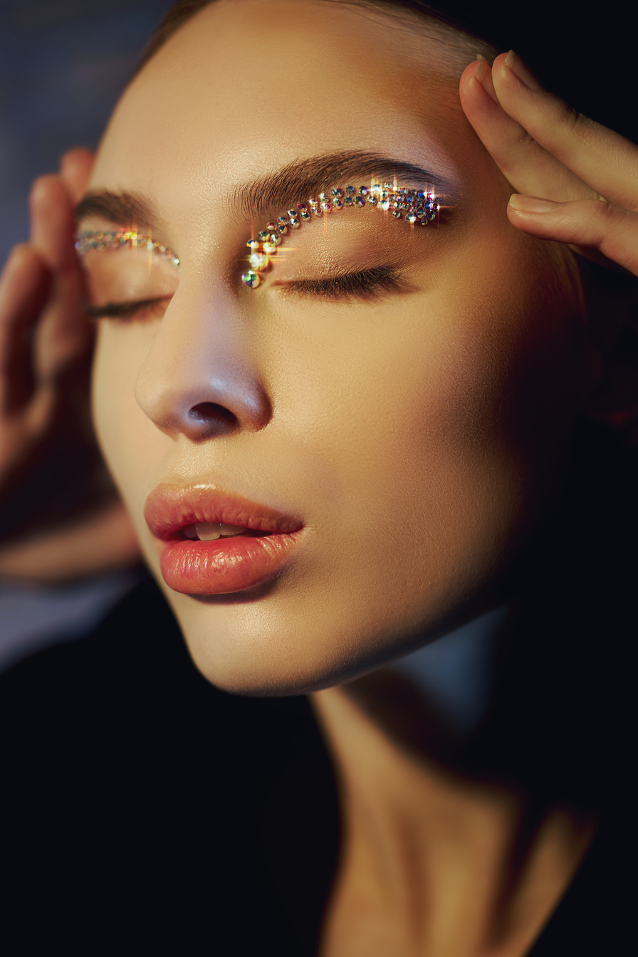 Beautiful eyebrows woman, rhinestones on eyes, professional makeup eyebrows on woman face. Shiny rhinestones on eyelid eyebrows